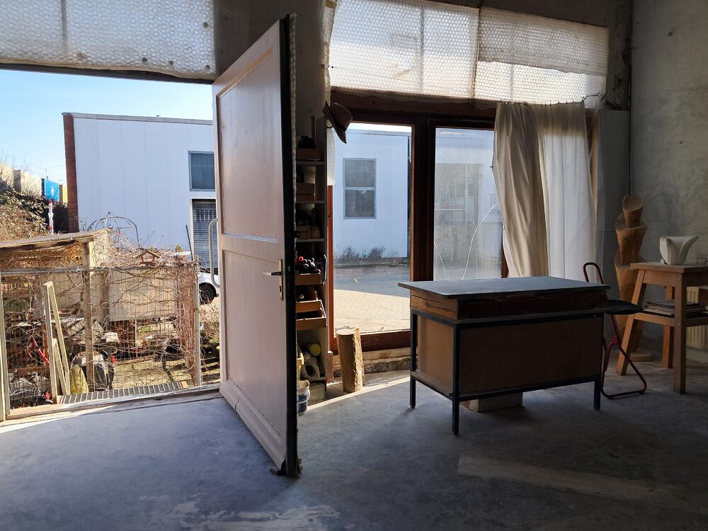 Rosas Atelier mit offenen Türen, vor dem Fenster ein Holztisch mit Stuhl und Utensilien.